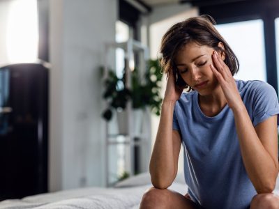 sad-woman-suffering-from-headache-sitting-bed-with-eyes-closed-while-holding-her-head-pain (1)